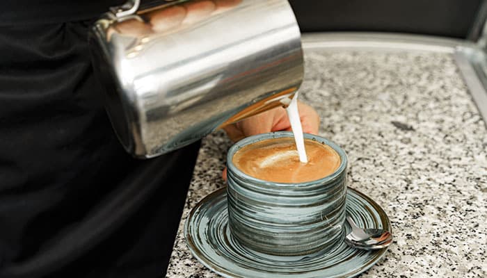 Barista poring milk into a coffee in a cafe in Headingley